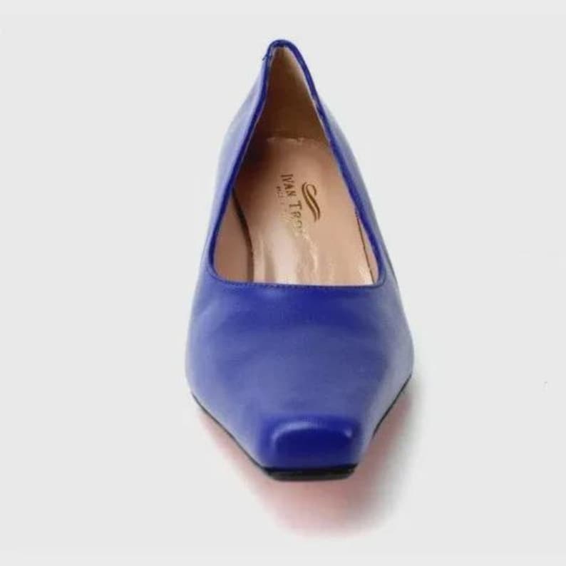 May include: A close-up of a blue leather pump with a square toe. The shoe has a low heel and a smooth, shiny finish. The interior of the shoe is a light tan color. The brand name "Ivan Troy" is visible inside the shoe.