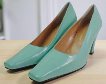 May include: A pair of mint green leather pumps with square toes and high heels. The shoes have a classic design, with a smooth, glossy finish. The interior is a light brown color.