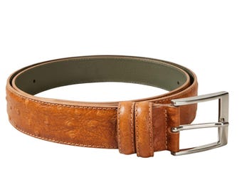 May include: A tan belt with a textured ostrich-like pattern and a silver-toned metal buckle. The belt features a smooth olive green interior lining and two matching tan leather loops near the buckle, creating a structured and functional accessory.
