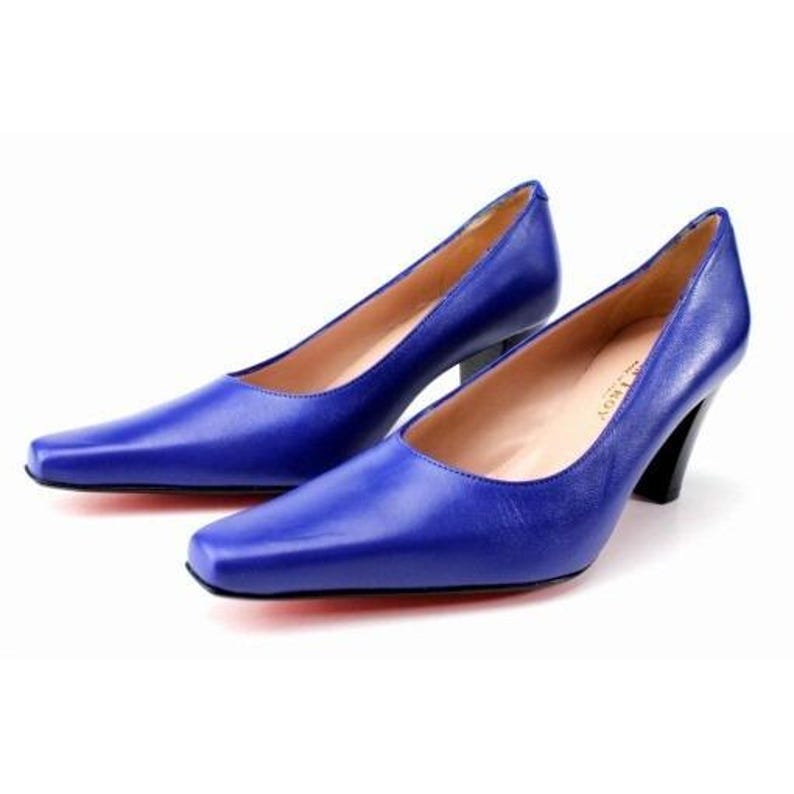 May include: A pair of cobalt blue leather pumps with a square toe and a black heel. The shoes have a classic design and are set against a white background. The heels are approximately 2.5 inches high.