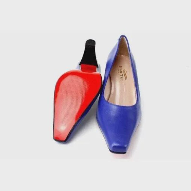 May include: A pair of blue leather pumps with a square toe and a high heel. The sole of one shoe is red. The heel is black. The interior of the shoe is tan with the text "IVAN TER" printed on the insole.