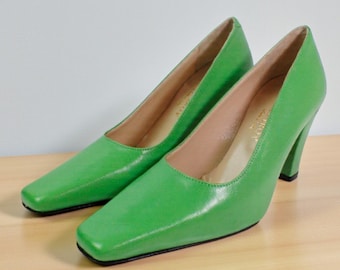 May include: A pair of bright green leather pumps featuring a square toe design, a moderate block heel, and a smooth finish. The interior lining is a light tan color with visible branding text printed on the heel bed of each shoe.
