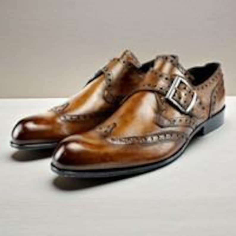 May include: A pair of brown leather monk strap shoes featuring a burnished finish, intricate brogue detailing along the seams, a pointed toe, and a silver-toned metal buckle closure on the side strap, set on a dark sole with a low heel.