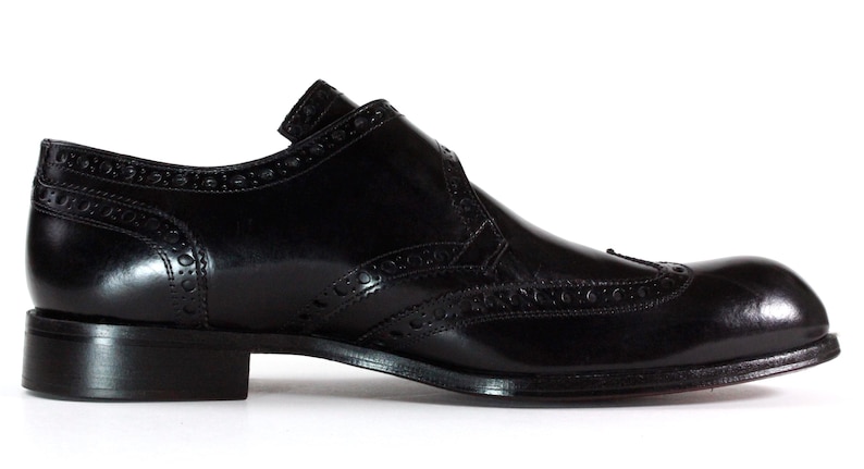 May include: A black leather oxford shoe featuring a wingtip design with decorative brogue perforations along the seams, a rounded toe, a low stacked heel, and a smooth polished finish on the exterior surface of the footwear.