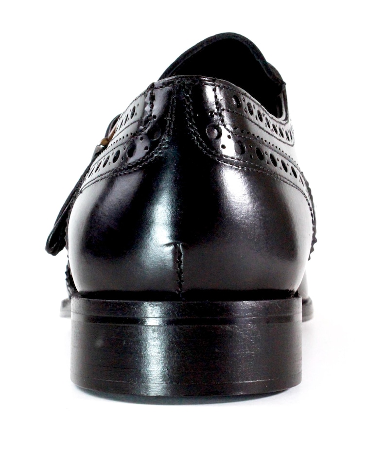 May include: A polished black leather dress shoe viewed from the back, featuring intricate brogue detailing along the heel counter and a stacked leather heel. The shoe has a smooth, glossy finish and a structured silhouette with visible stitching.