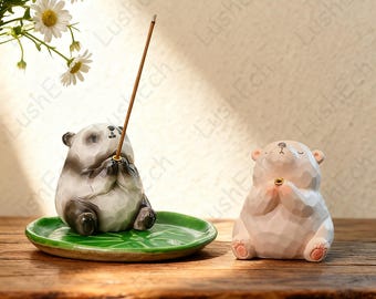 May include: Two ceramic figurines: a panda and a bear, both in a meditative pose. The panda is black and white, holding an incense stick above a green leaf-shaped dish. The bear is white with pink accents. Both have closed eyes and clasped hands.