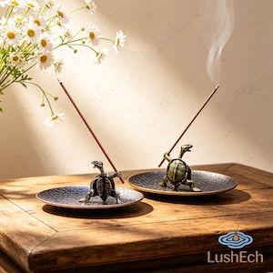 May include: Two bronze-colored turtle incense holders, each positioned on a circular tray with a textured, dark, scale-like pattern. Each turtle figure holds a single lit incense stick, with thin trails of smoke rising into the air.