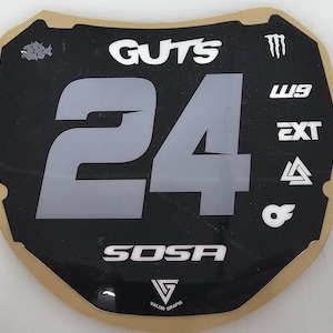 May include: Black and gray number plate with the number 24 in large gray font. The word "GUTS" is at the top, and "SOSA" is at the bottom. Various logos and text are also present.