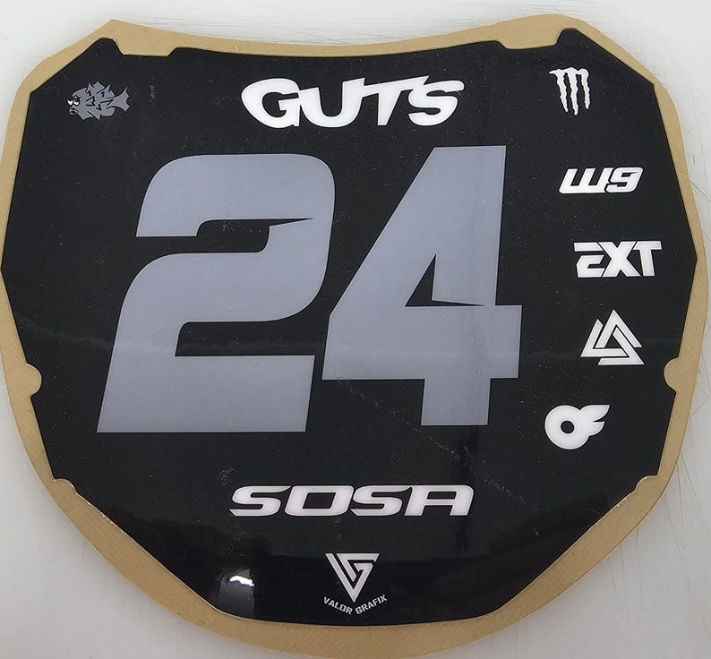 May include: Black and gray number plate with the number 24 in large gray font. The word "GUTS" is at the top, and "SOSA" is at the bottom. Various logos and text are also present.