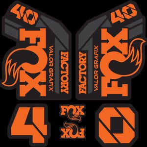 May include: A collection of black and orange Fox Factory decals. The decals include the number "40", the word "FOX" with a fox tail graphic, and the words "FACTORY" and "VALOR GRAFIX". The decals are designed for mountain bikes.