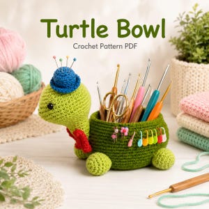 May include: A green crocheted turtle bowl with a blue hat on its head, serving as a pincushion. The turtle's shell acts as a container for various metal crochet hooks and scissors, with colourful stitch markers attached to the side. Text reads Turtle Bowl Crochet Pattern PDF.