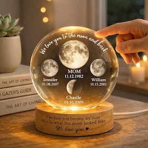 May include: A clear glass sphere with moon phase images and names, resting on a wooden base. The sphere has the text "We love you to the moon and back." The base reads "The date you became my mom this is what the moon looked like We love you."