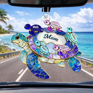 May include: A decorative car charm shaped like a sea turtle, featuring a mosaic design in shades of blue, purple, and green. The charm has the word "Mom" in the center, surrounded by smaller turtles with names. It hangs from a silver chain.