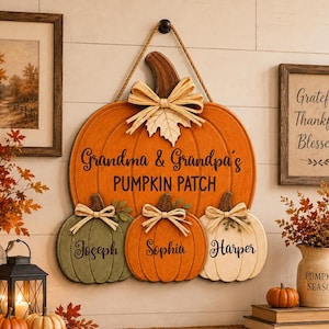 May include: A wooden wall hanging shaped like a large orange pumpkin with the text Grandma & Grandpa's PUMPKIN PATCH. Three smaller pumpkins in green, orange, and white are attached below, each featuring the names Joseph, Sophia, and Harper.