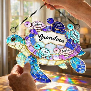 May include: Stained glass turtle suncatcher with the word "Grandma" and the names Ashley, Lucas, Charles, Peter, and Sophia. The turtle is in shades of blue, purple, and green, with a black chain for hanging.