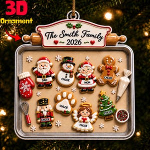 May include: A 3D Christmas ornament shaped like a baking sheet with a rolling pin top. It features gingerbread-style figures of Santa, a snowman, a woman, a gingerbread man, a nutcracker, an angel, a paw print, a tree, a mitten, a whisk, and icing.
