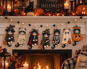 May include: A decorative garland featuring seven wooden cat ornaments dressed in various Halloween costumes, including a witch, mummy, vampire, skeleton, ghost, and pumpkin, strung together on a twine cord with alternating black and white beads.