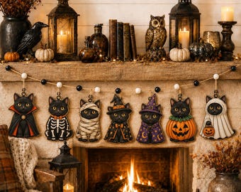 May include: A Halloween garland featuring seven hanging wooden ornaments of black cats in various costumes, including a vampire, skeleton, mummy, witch, wizard, pumpkin, and ghost, strung on a twine cord with alternating black and white beads.