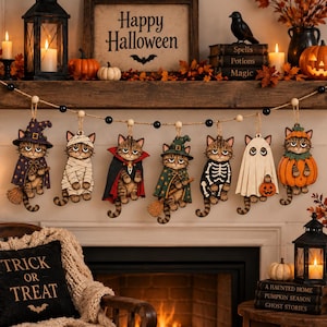 May include: A decorative garland featuring seven hanging wooden cat ornaments, each dressed in a different Halloween costume including a witch, mummy, vampire, skeleton, ghost, and pumpkin, suspended on a string with black and wooden beads.