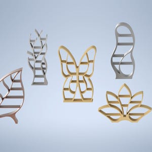 May include: A collection of decorative metal shelves in various nature-inspired shapes. The designs include a leaf, a butterfly, a lotus flower, and abstract forms. The shelves are in shades of gold, silver, and bronze, set against a light blue background.