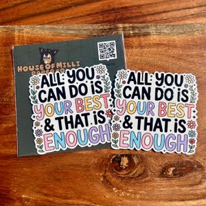 Puede incluir: Dos pegatinas con el texto "ALL YOU CAN DO IS YOUR BEST & THAT IS ENOUGH" en letras coloridas, rodeadas de dise&ntilde;os florales. Una tarjeta de visita con una ilustraci&oacute;n de perro y un c&oacute;digo QR est&aacute; detr&aacute;s de las pegatinas.