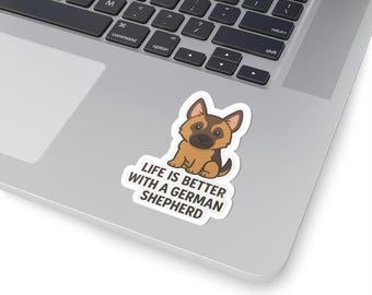 May include: A sticker featuring a cartoon German Shepherd puppy in brown and black, with the text "LIFE IS BETTER WITH A GERMAN SHEPHERD" in black on a white background. The sticker is on a laptop.