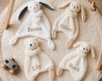 May include: Four plush security blankets featuring stuffed animal heads and limbs. One white rabbit with black and white striped ears is embroidered with Emma. Three cream-colored plush toys, a rabbit and two bears, are embroidered with Oliver, Lily, and Noah.