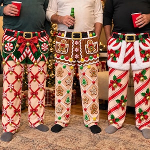 May include: Three pairs of festive holiday pants featuring Christmas themes. The left pair has elf-style green and red accents with peppermint candies. The center pair features gingerbread men and icing details. The right pair displays candy cane stripes.