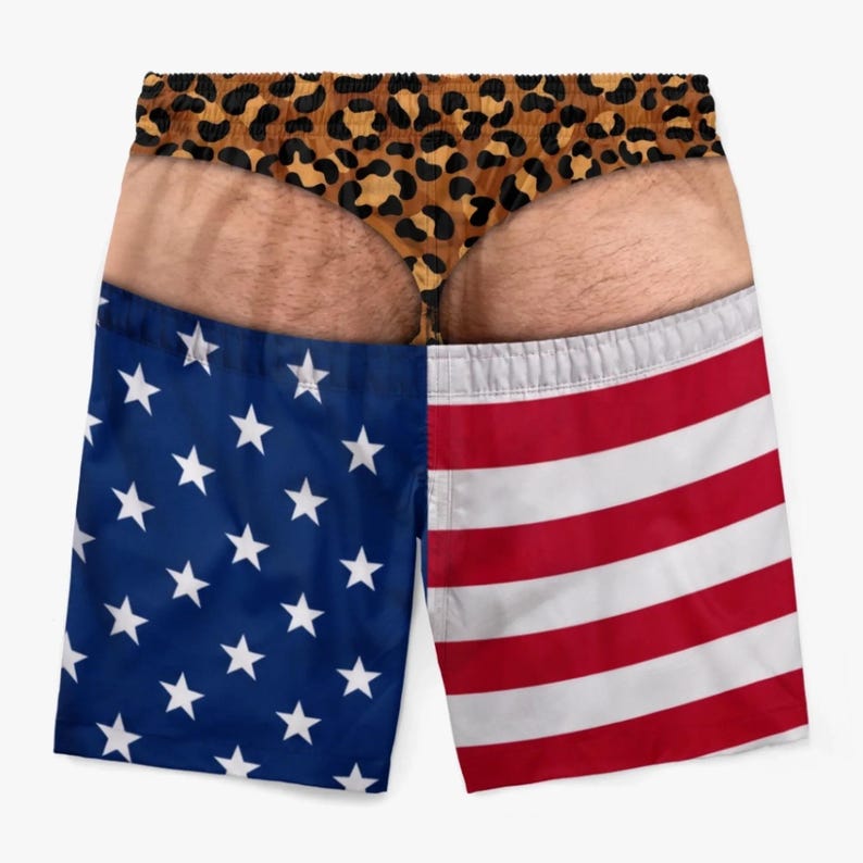 May include: Swim trunks featuring a realistic photographic print of a person's lower back and buttocks wearing a leopard print thong. The lower portion of the trunks displays the American flag pattern with white stars on blue and red and white stripes.