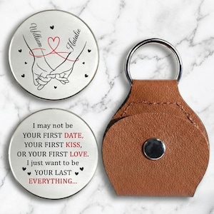 May include: A set of personalized gifts, including two silver-colored round tokens with names and a heart design, and a brown leather keychain. One token reads "I may not be your first date..." with a heart symbol.