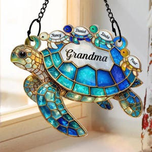 May include: A decorative stained glass turtle with the word "Grandma" and the names "Nancy", "Daniel", "Linda", and "Paul". The turtle is primarily blue and teal with gold accents, hanging from a black chain.