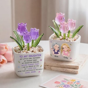 Puede incluir: Dos macetas de cerámica blanca con flores de tulipanes de cristal. Una maceta tiene tulipanes morados y el texto "To My Daughter". La otra maceta tiene tulipanes rosas e ilustraciones de una madre y una hija.