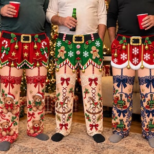 May include: Three pairs of festive holiday pajama pants featuring a printed belt design at the waist. The left pair is red with teddy bears, the center pair is green with gingerbread men, and the right pair is red with toy trains and blue lace.
