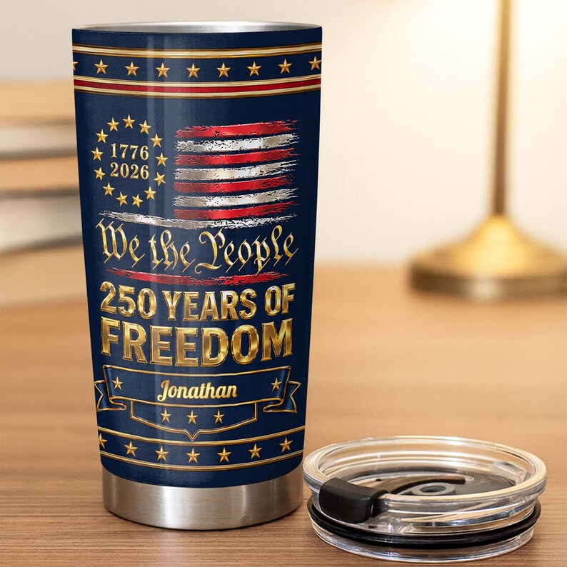 May include: A navy blue stainless steel tumbler featuring a patriotic design with a distressed American flag, the text 1776 2026, We the People, 250 YEARS OF FREEDOM, and the name Jonathan. The tumbler includes a clear plastic lid with a black slider.
