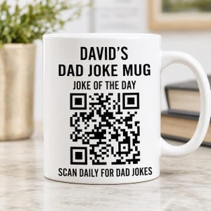May include: A white ceramic mug featuring black text that reads DAVID'S DAD JOKE MUG, JOKE OF THE DAY, and SCAN DAILY FOR DAD JOKES. A large black and white QR code is printed in the center of the mug, positioned between the top and bottom text lines.