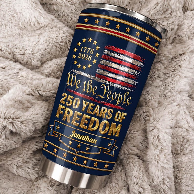 May include: A navy blue stainless steel tumbler featuring a gold and red American flag design with stars. Text reads: 1776 2026, We the People, 250 YEARS OF FREEDOM, and the name Jonathan. The tumbler has a metallic silver rim and base.