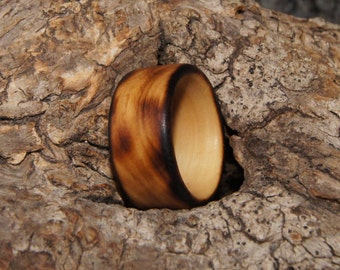 Puede incluir: Un anillo de madera con un acabado quemado marrón oscuro y un interior marrón claro. El anillo está sentado sobre un trozo de corteza de árbol.
