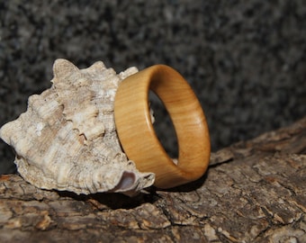 Puede incluir: Un anillo de madera con un acabado de veta de madera natural. El anillo es de color marrón claro y tiene una superficie lisa y pulida.