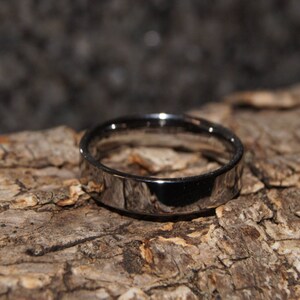 May include: A silver wedding band with a smooth, polished finish. The band is thick and has a slightly rounded edge.