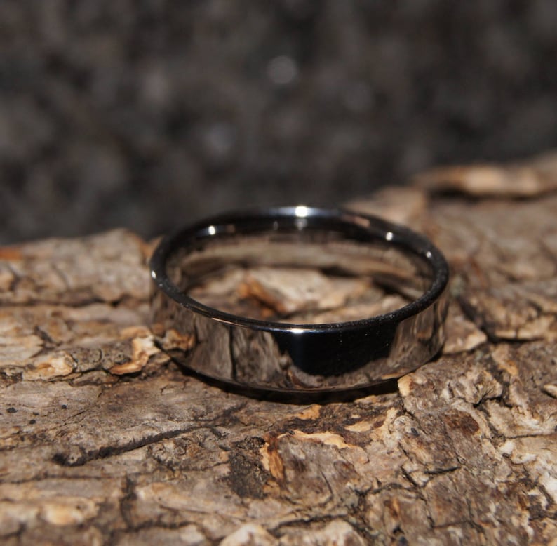 May include: A silver wedding band with a smooth, polished finish. The band is thick and has a slightly rounded edge.