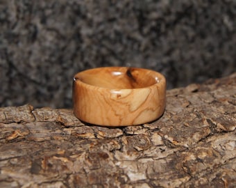 Puede incluir: Un anillo de madera hecho de madera de olivo. El anillo tiene un patrón de veta de madera natural y es de color marrón claro.