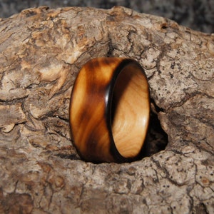 Op de afbeelding: Een houten ring met een donkerbruine buitenrand en een lichtbruine binnenrand. De ring is gemaakt van hout en heeft een natuurlijke afwerking.