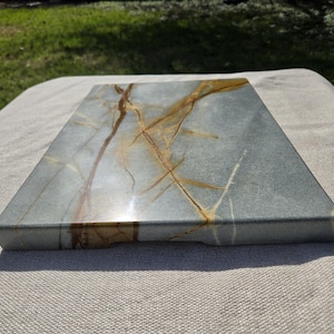 May include: A rectangular stone serving board featuring a smooth, polished surface with a cool gray base color and prominent, intricate golden-brown veining patterns that stretch across the entire top face of the slab.