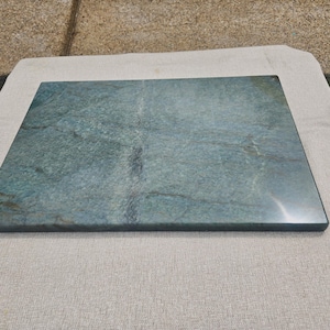 May include: A rectangular stone slab featuring a polished surface with a deep teal and blue-green color palette. The natural stone displays intricate veining patterns in darker shades of gray and black, creating a textured appearance.