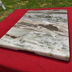 May include: A rectangular stone serving board featuring a polished surface with swirling patterns of white, sage green, and dark brown. The slab has a smooth, flat top and straight edges, showcasing natural mineral veining throughout the material.