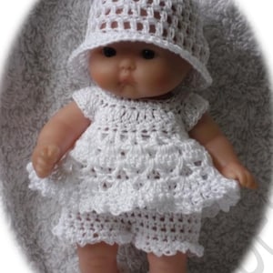May include: A white crocheted outfit for a baby doll, including a hat, dress, shorts, and booties.
