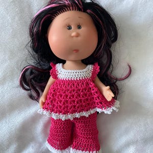 Könnte beinhalten: Eine gehäkelte Puppe in einem rosa-weißen Outfit. Die Puppe hat langes schwarzes Haar mit pinkfarbenen Strähnen und große braune Augen.
