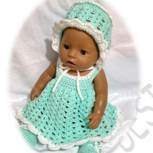 May include: A crocheted baby doll outfit in a light green color with white trim. The outfit includes a dress, hat, and booties.