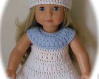 May include: A white crocheted dress with a blue crocheted collar and a white crocheted hat. The dress has a simple design and is perfect for a doll.
