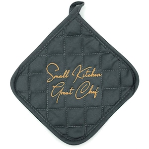 Op de afbeelding: Donkergrijze gewatteerde pannenlap met een ophanglus. De pannenlap heeft de geborduurde tekst "Small Kitchen Great Chef" in een goudkleurig script. De pannenlap is ruitvormig.